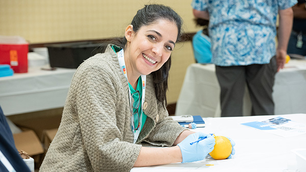 Doctor practicing sutures on orange while smiling at camera